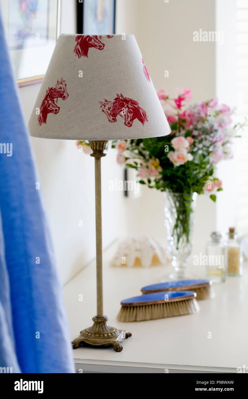 Close-up of lamp with cream linen lampshade with red horse motif on dressing table ith blue enamelled brushes Stock Photo