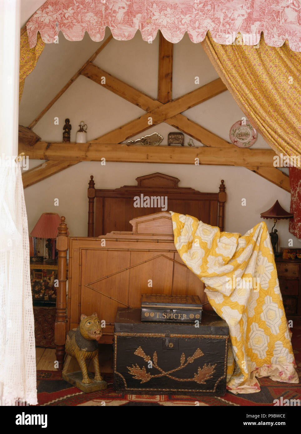 Yellow patterned throw on pine bed in attic bedroom with antique painted chest and pine beams Stock Photo