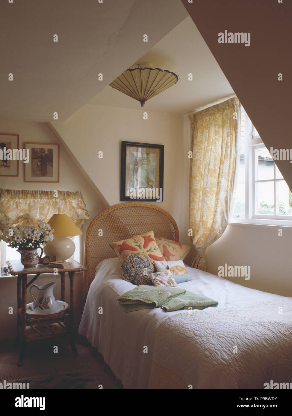 Bamboo table beside single bed below window in attic cottage bedroom Stock Photo