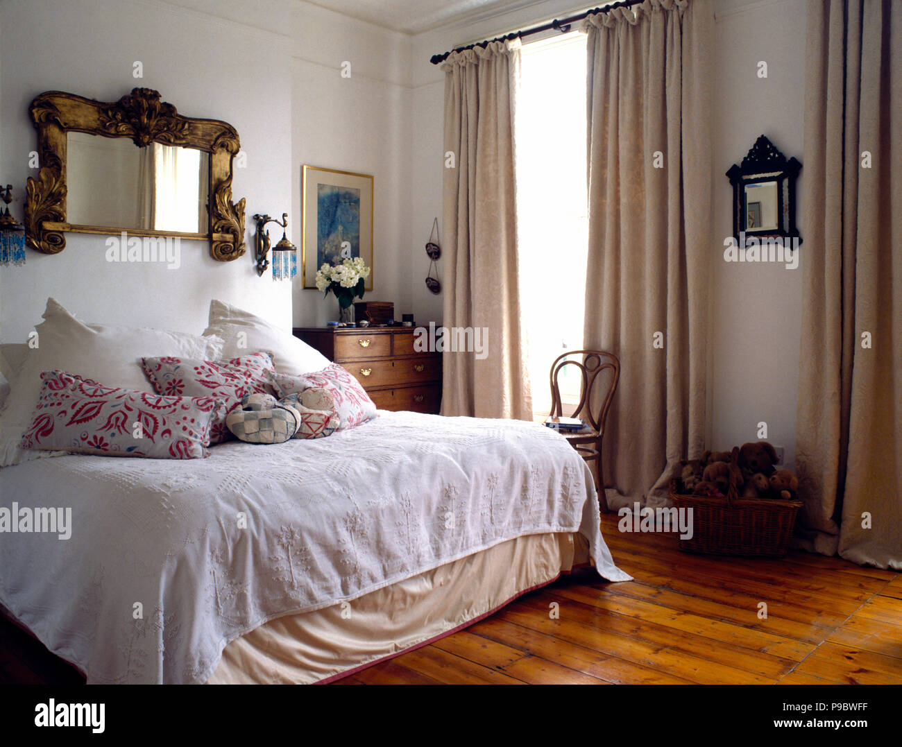 Antique mirror above bed with vintage cotton bedspread in townhouse bedroom with cream curtains and a wooden floor Stock Photo