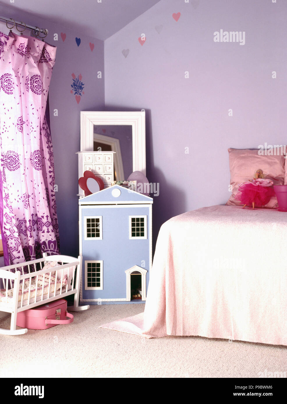Blue dolls' house and mauve curtains in child's lilac bedroom Stock Photo