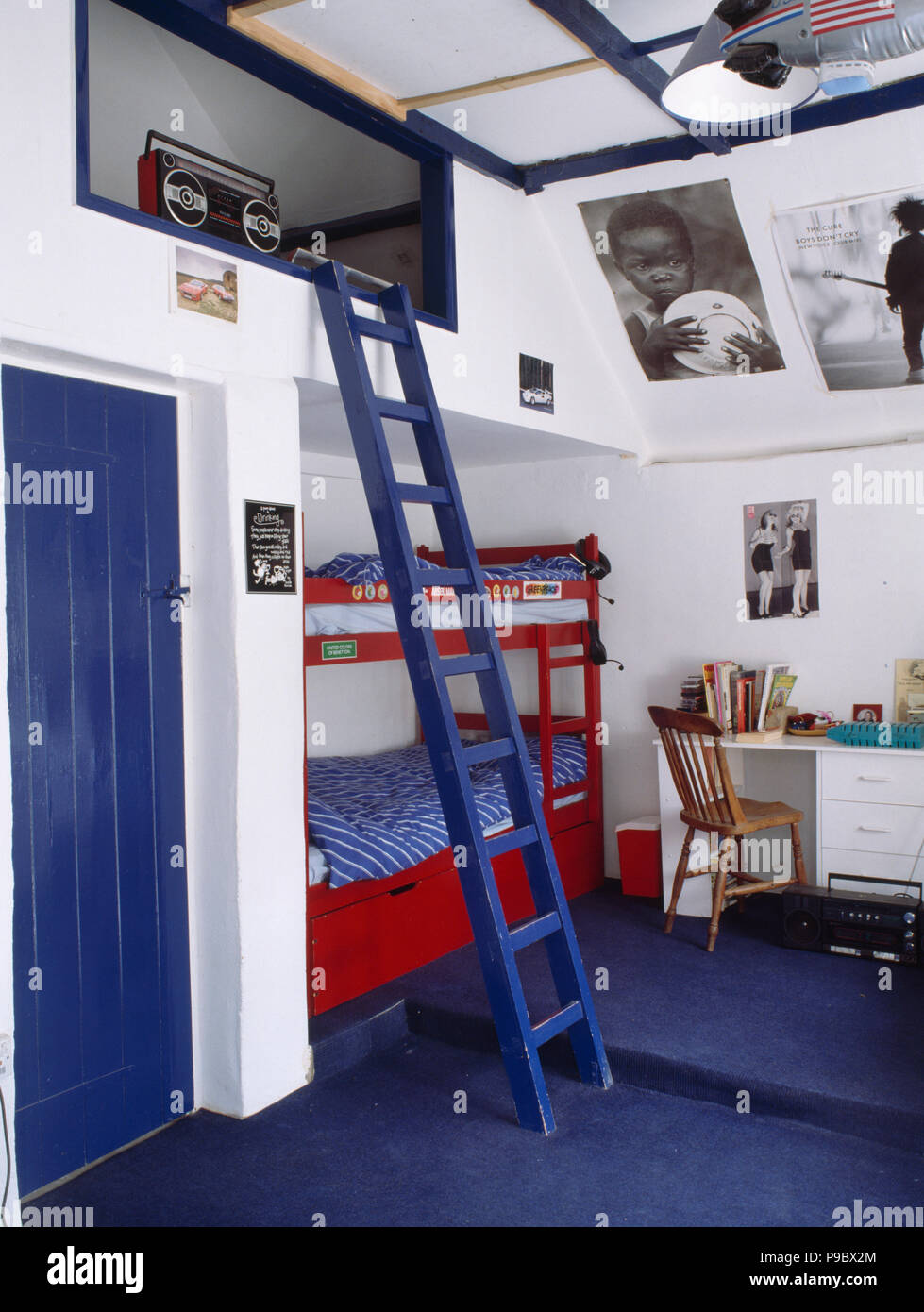 Red bunk beds with blue linen in childs bedroom with blue ladder and carpet Stock Photo