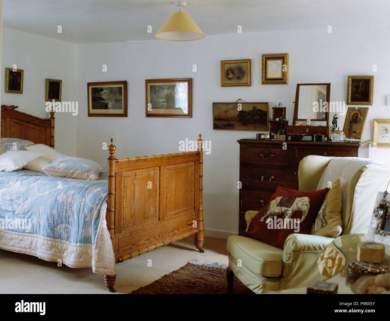 Blue+white quilt on antique wooden bed in white cottage bedroom with cream armchair Stock Photo
