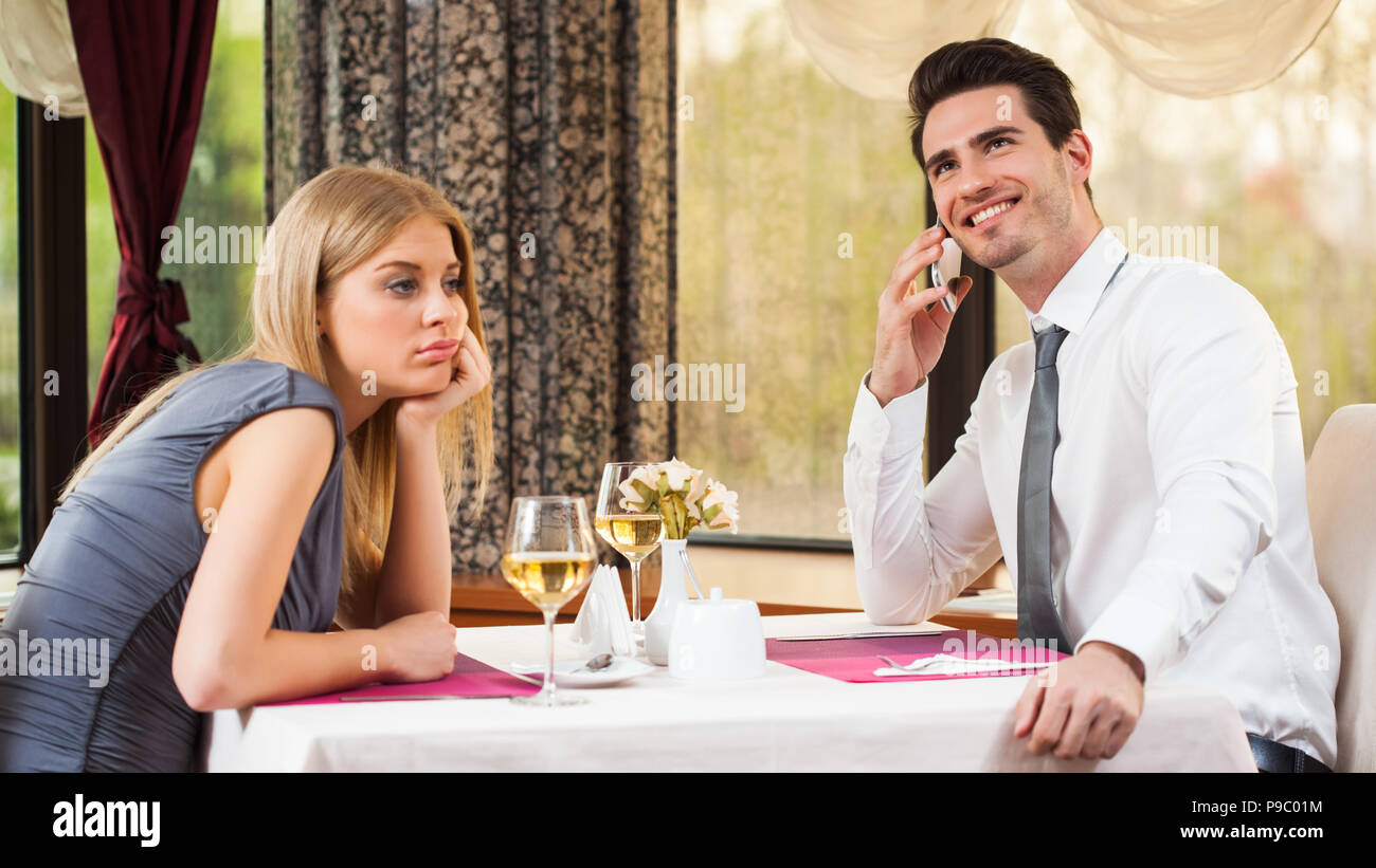 Woman is bored at restaurant, her boyfriend talks on the phone Stock Photo