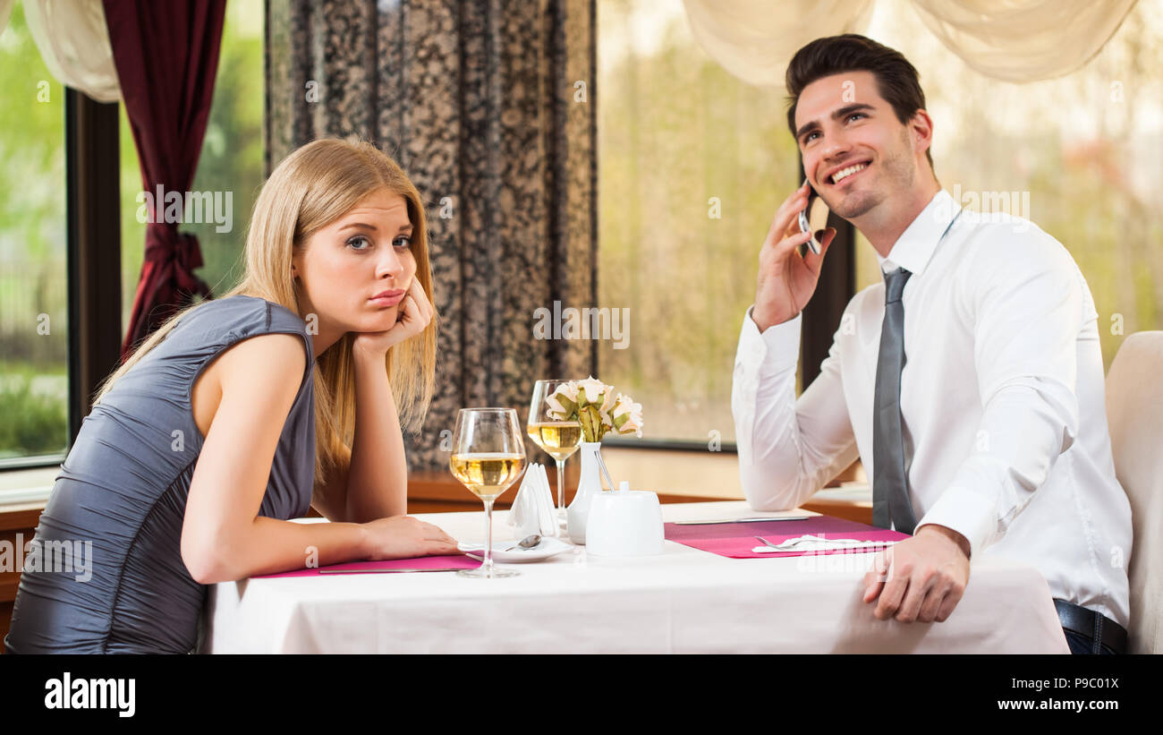 Woman is bored at restaurant, her boyfriend talks on the phone Stock Photo