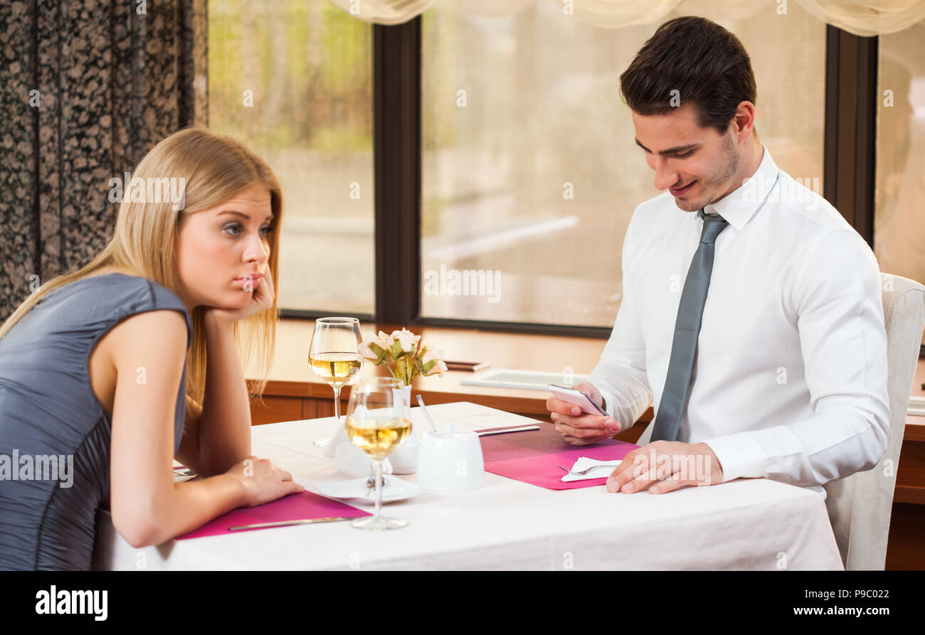 Woman is bored at restaurant, her boyfriend is typing sms Stock Photo