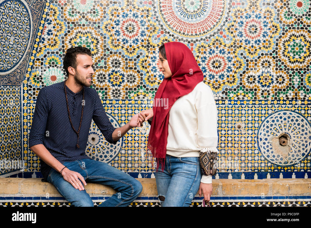 Young Muslim couple in relationship talking and smiling holding hands in front of arabesque oriental decoration Stock Photo