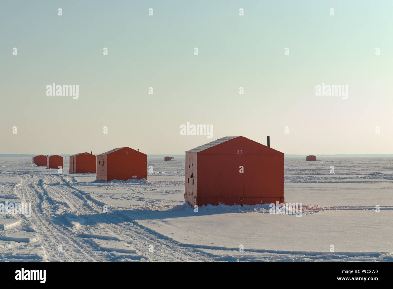 Orange Ice fishing huts on a frozen lake in Ontario at sunset showing tracks Stock Photo