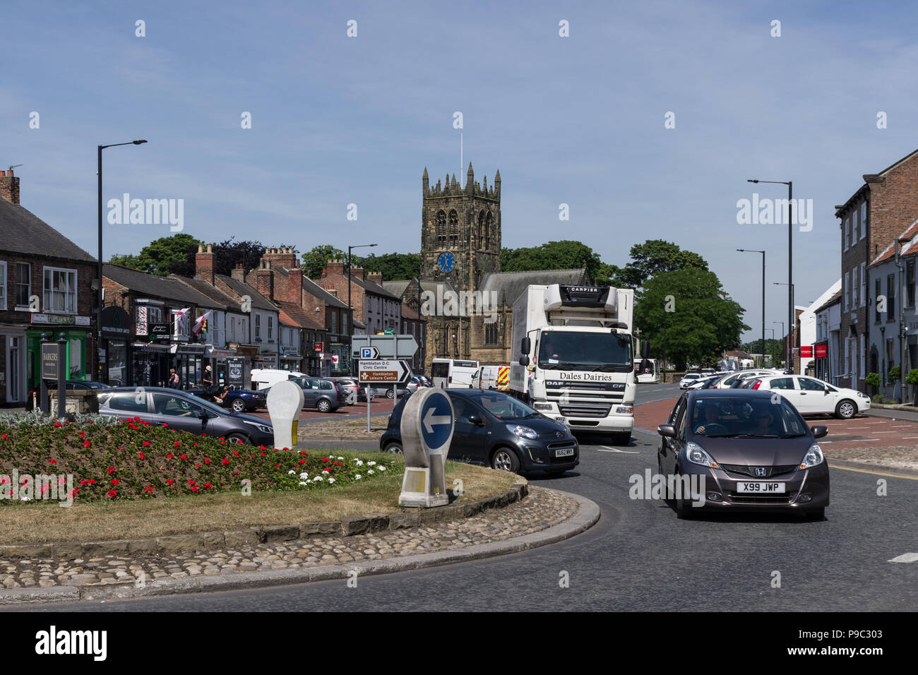 Traffic on the roundabout on Northallerton High Street with the historic church of All Saints in the background; North Yorkshire, UK Stock Photo