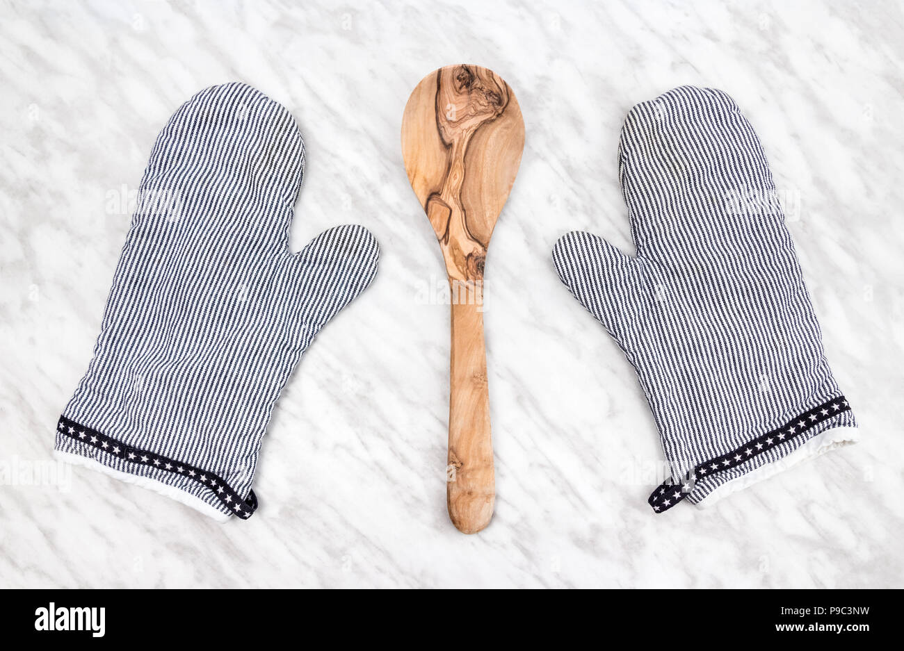 Wooden spoon and striped kitchen gloves, on a marble countertop. Stock Photo