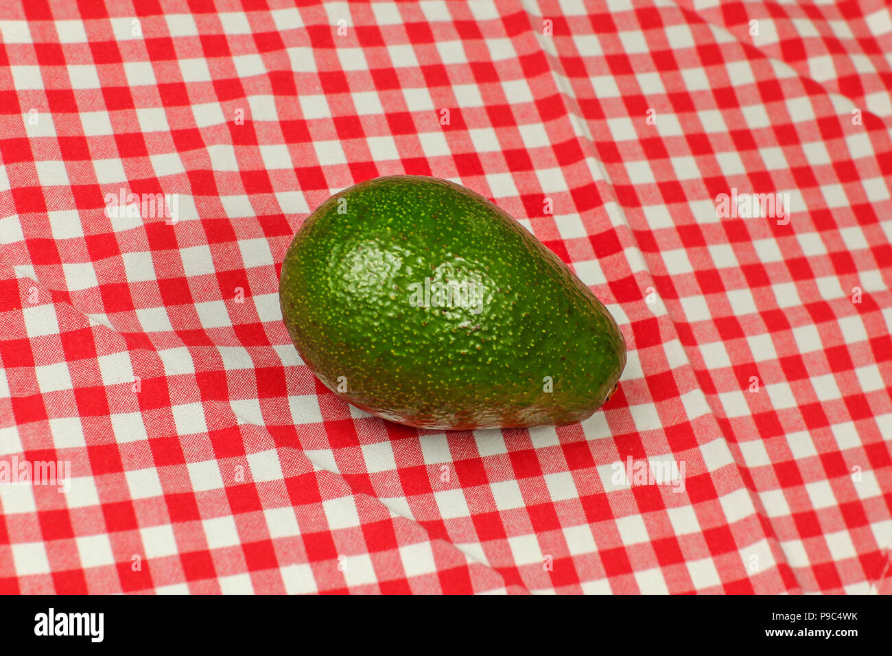 Whole avocado on red checkered tablecloth Stock Photo