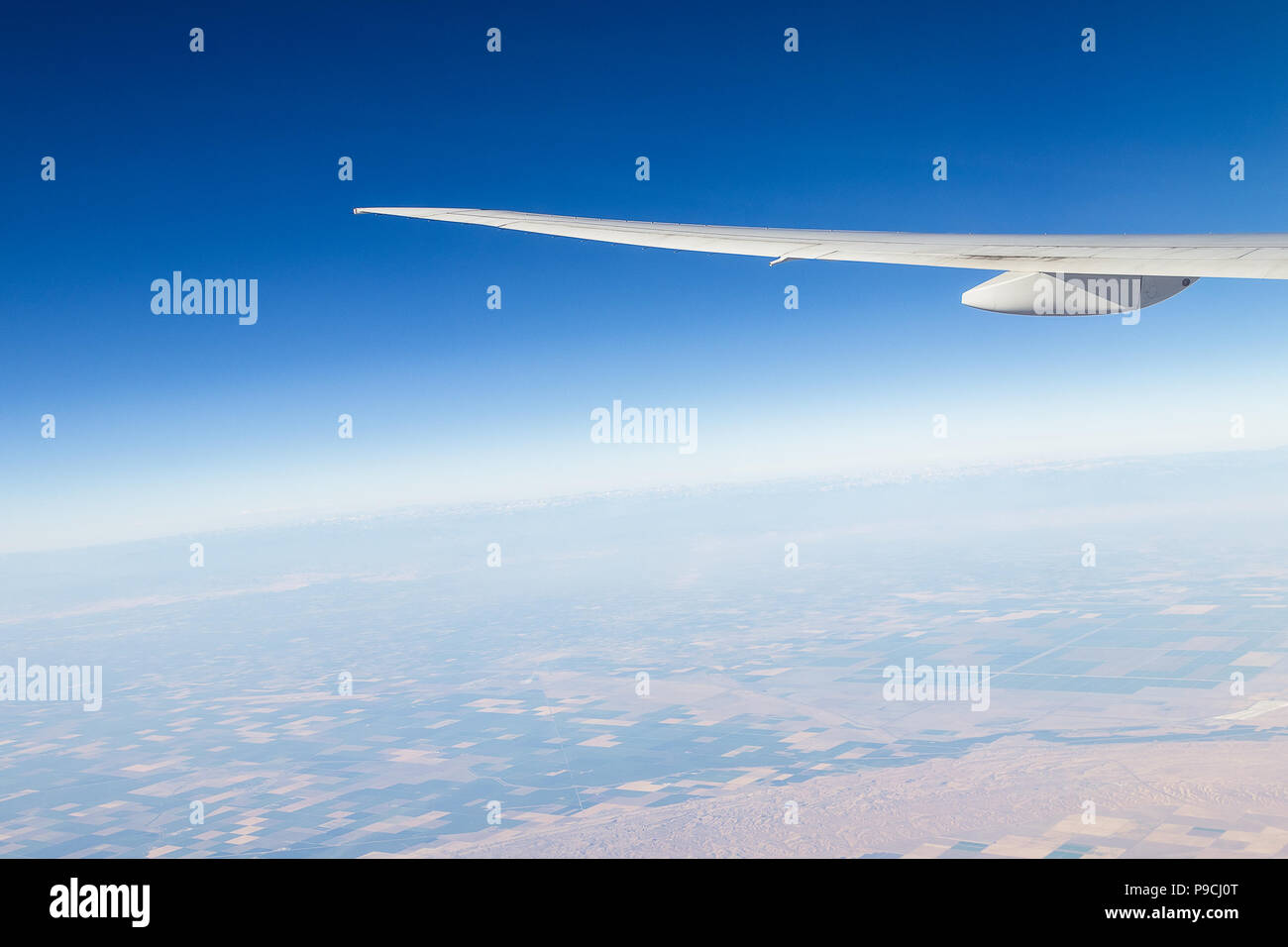 Air plane wing with blue sky and valley below. Stock Photo