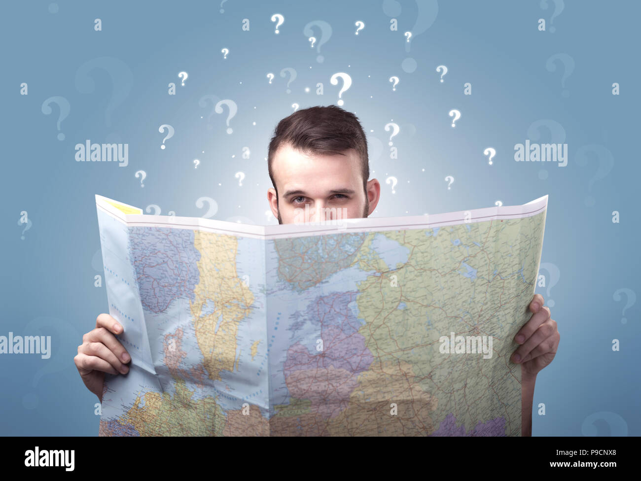 Handsome young man holding a map with white question marks above his ...