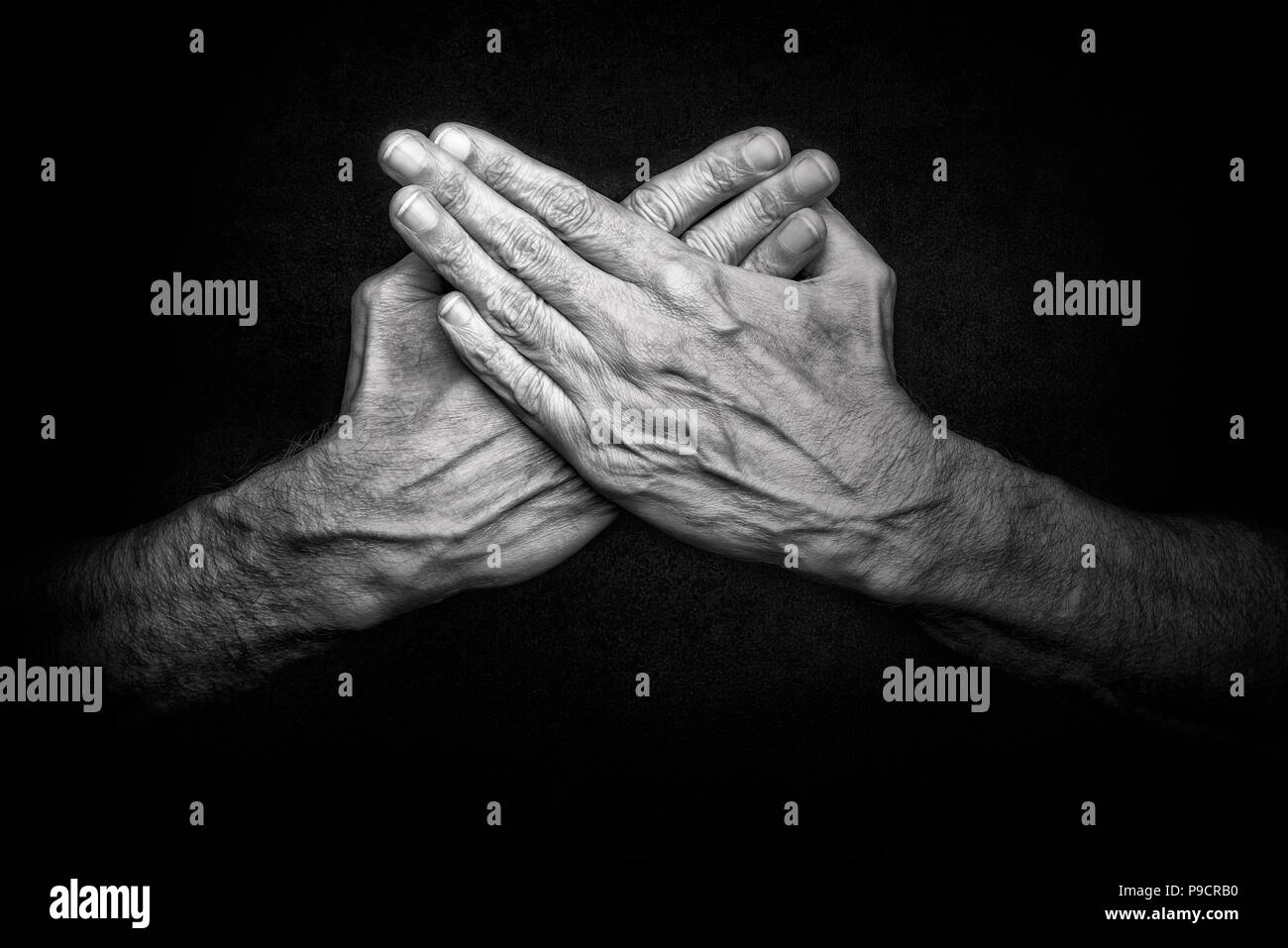 Black and White photo of crossed man's hands on dark background, symbolizing protection of security Stock Photo