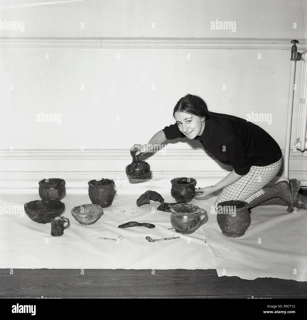 1960s, historical, archaeology, young female archaelogist with a display of archaeological or recovery artifacts, including ancient pots and bowls. The science  of archaeolgy grew out of the older multi-disciplinary study known as antiquarianism, the desire to learn more about past societies and the development of the human race. Stock Photo
