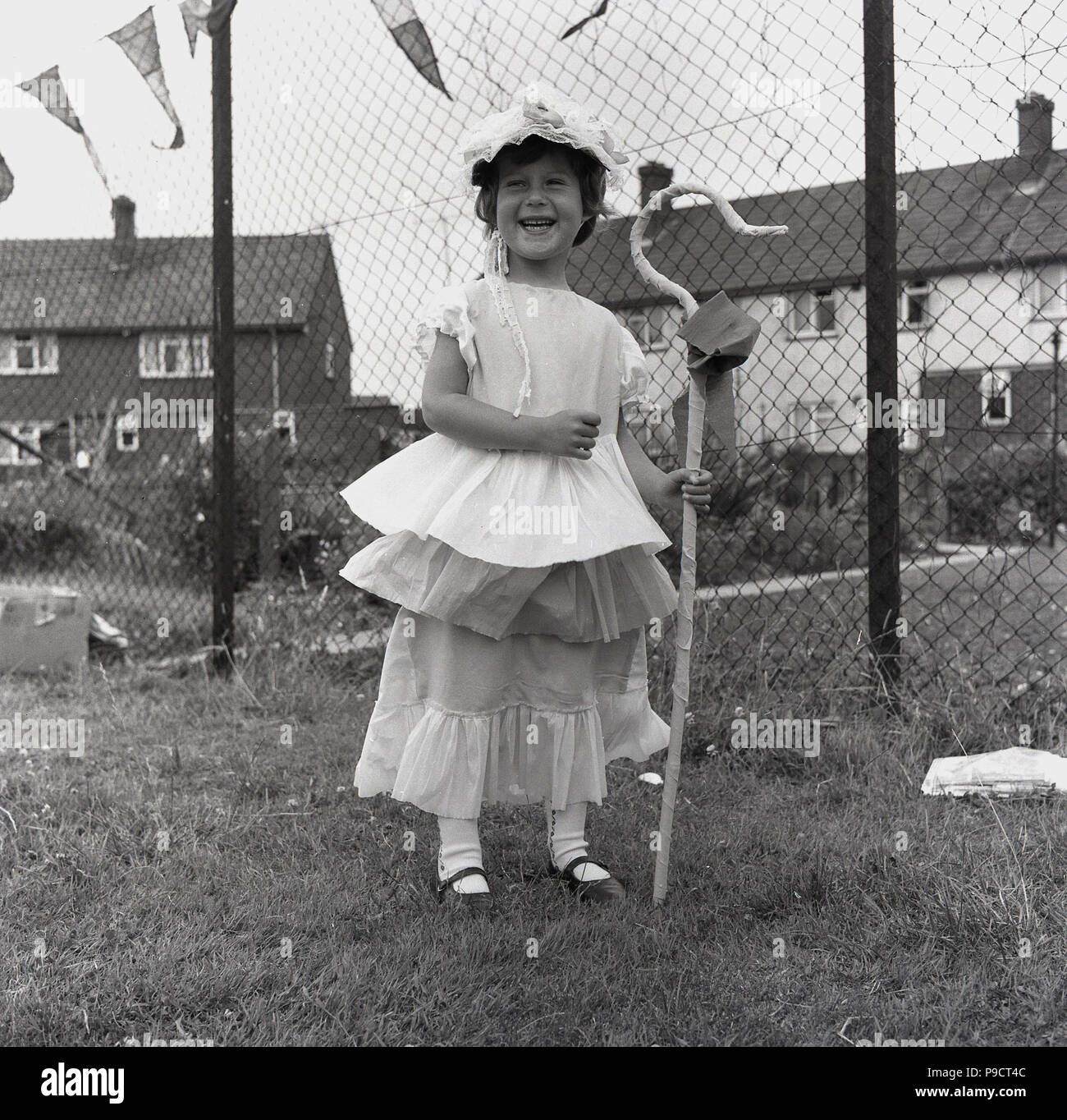 1960s, historical, happy young girl standing outside in a garden dressed in a 'little bo peep' costume, with hat and crook, England, UK. Little Bo Peep, a young shepherdress, was a character from a popular Engllish language nursey rhyme. Stock Photo