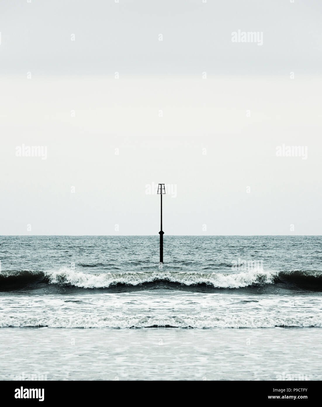 Waves and surf breaking onto a beach around a groyne beacon, England UK - symmetry concept Stock Photo