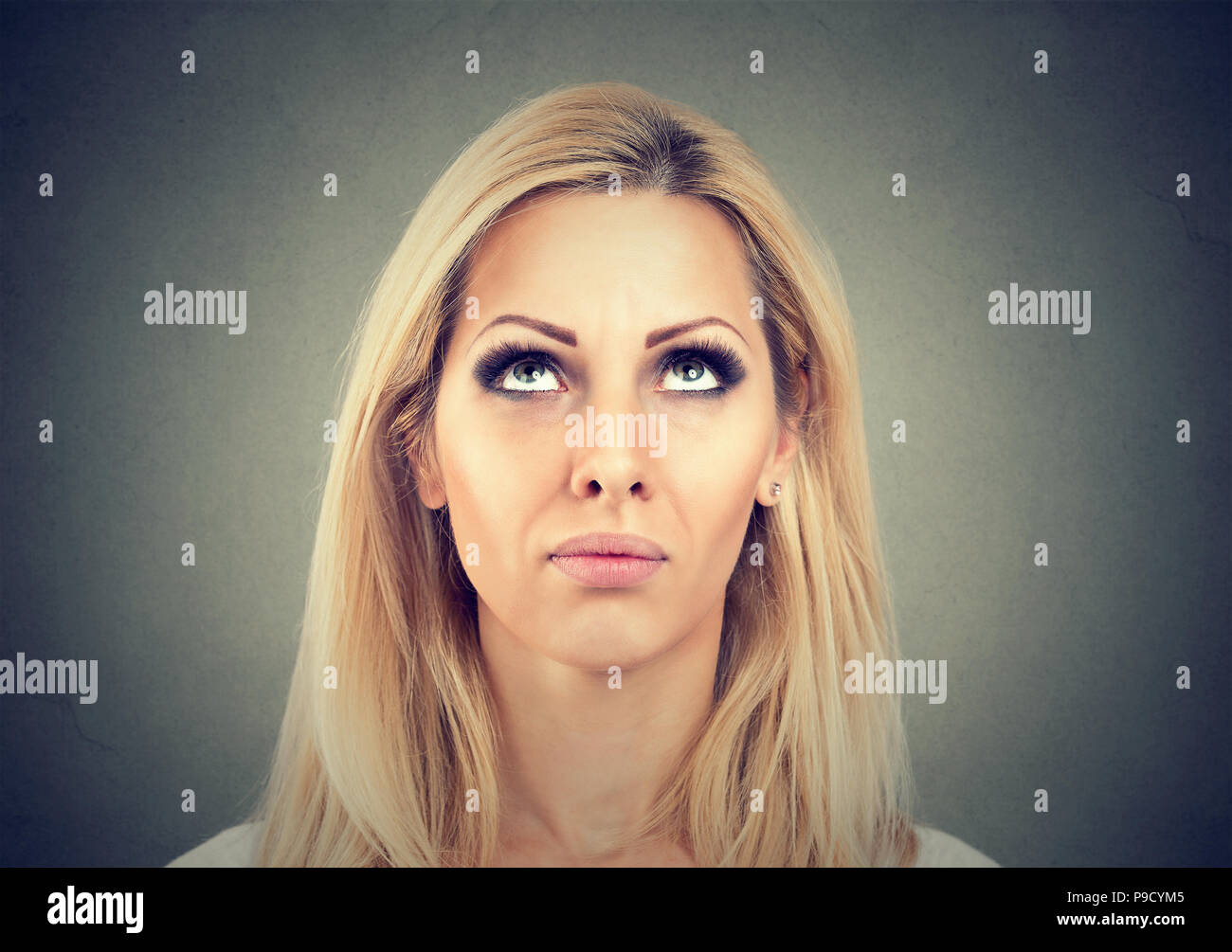 Blond woman looking up and thinking in mindfulness having doubts while making decision on gray background Stock Photo