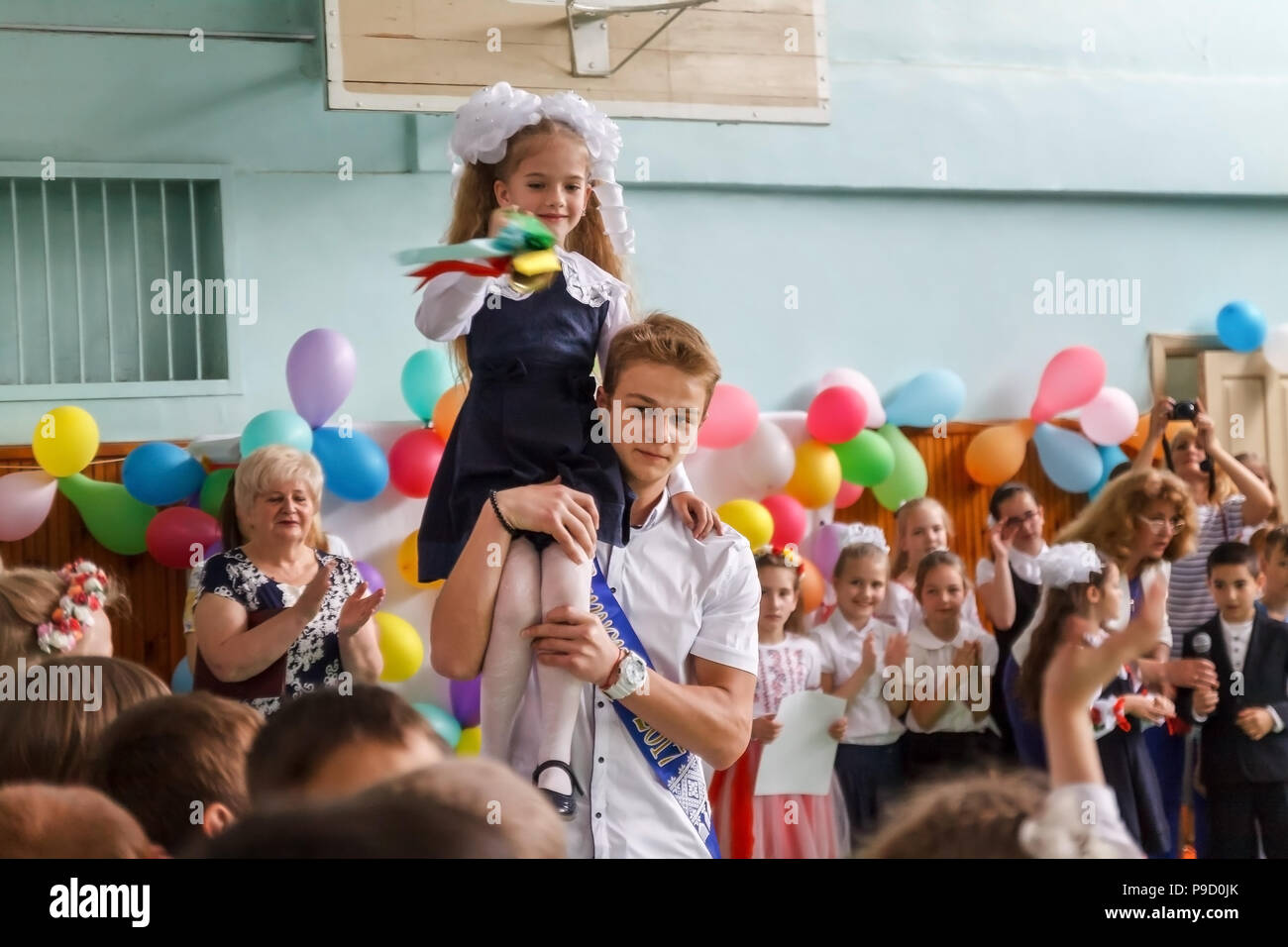 Kiev. Ukraine. May, 26. 2017- The last bell in high school. The graduate bears a first-grader girl on her shoulder with a big bell Stock Photo