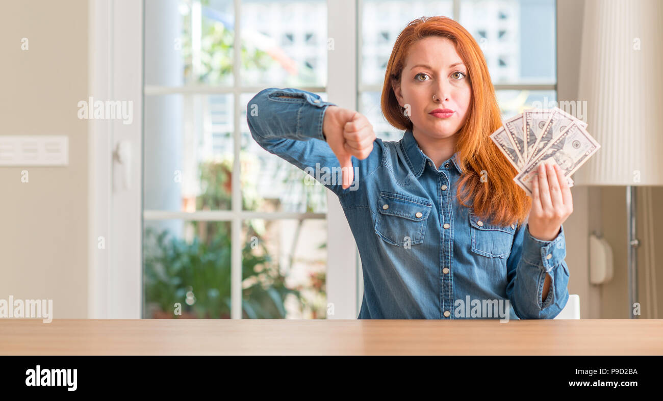 Redhead woman holding dollar bank notes at home with angry face ...
