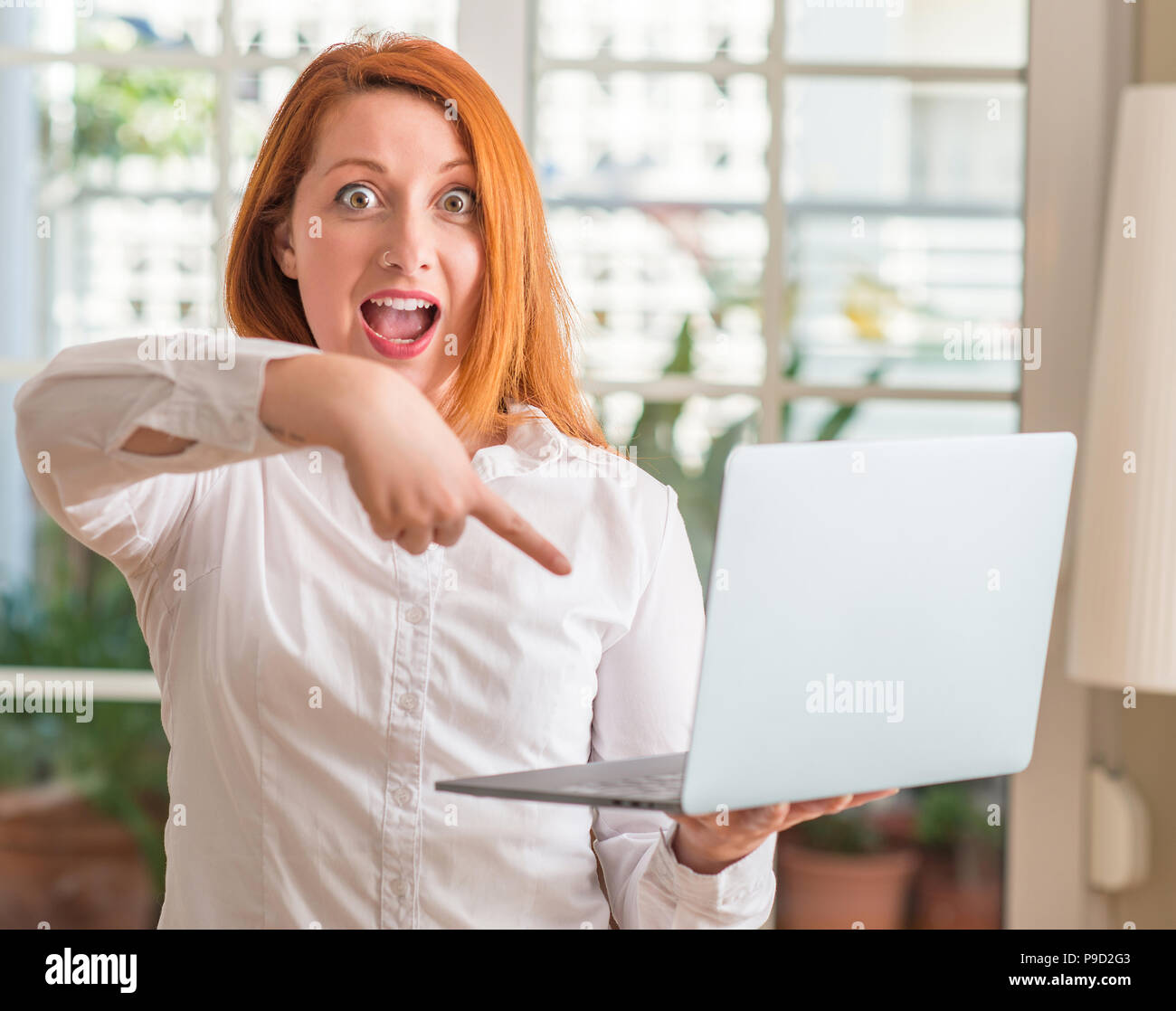 Redhead woman using computer laptop at home very happy pointing with ...