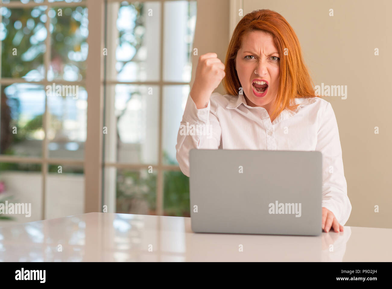Redhead woman using computer laptop at home annoyed and frustrated ...