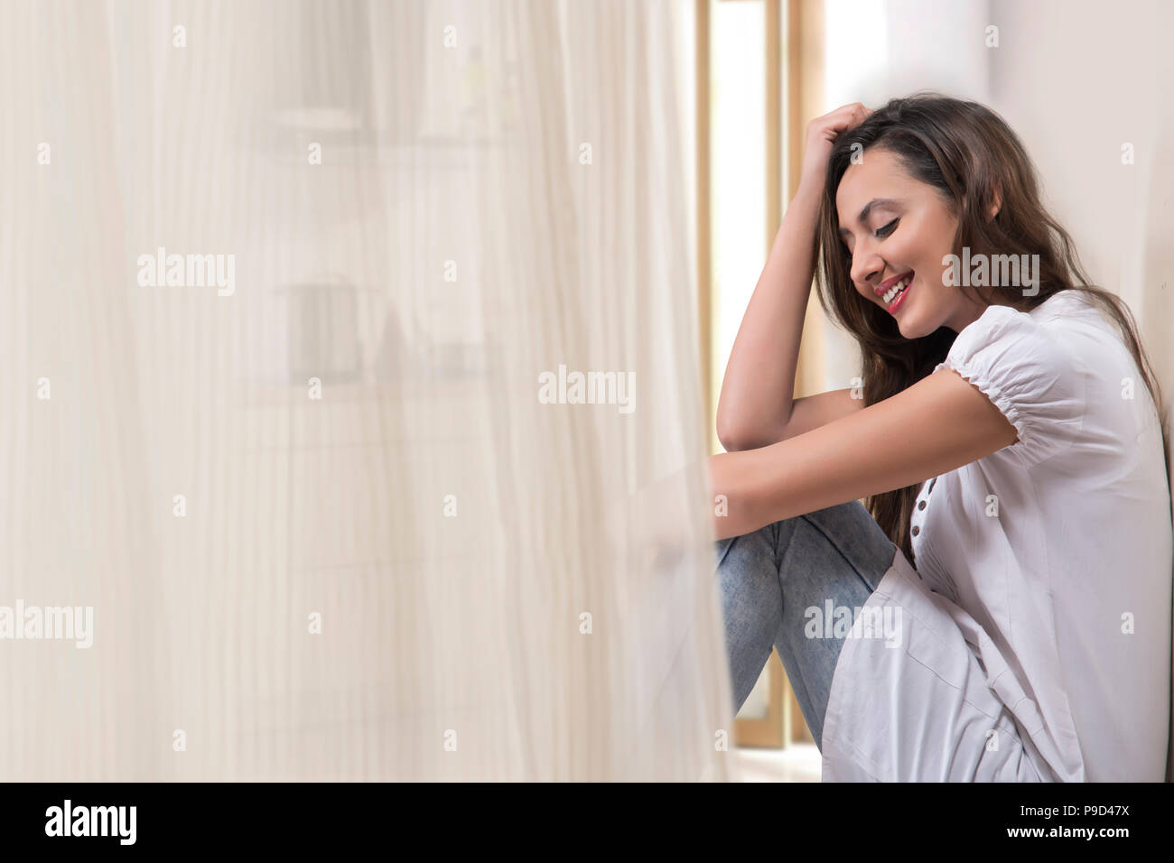 Young woman sitting against white wall at home Stock Photo