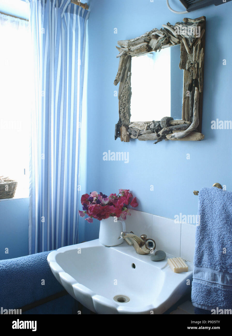 Driftwood framed mirror above white basin in pastel blue bathroom Stock Photo