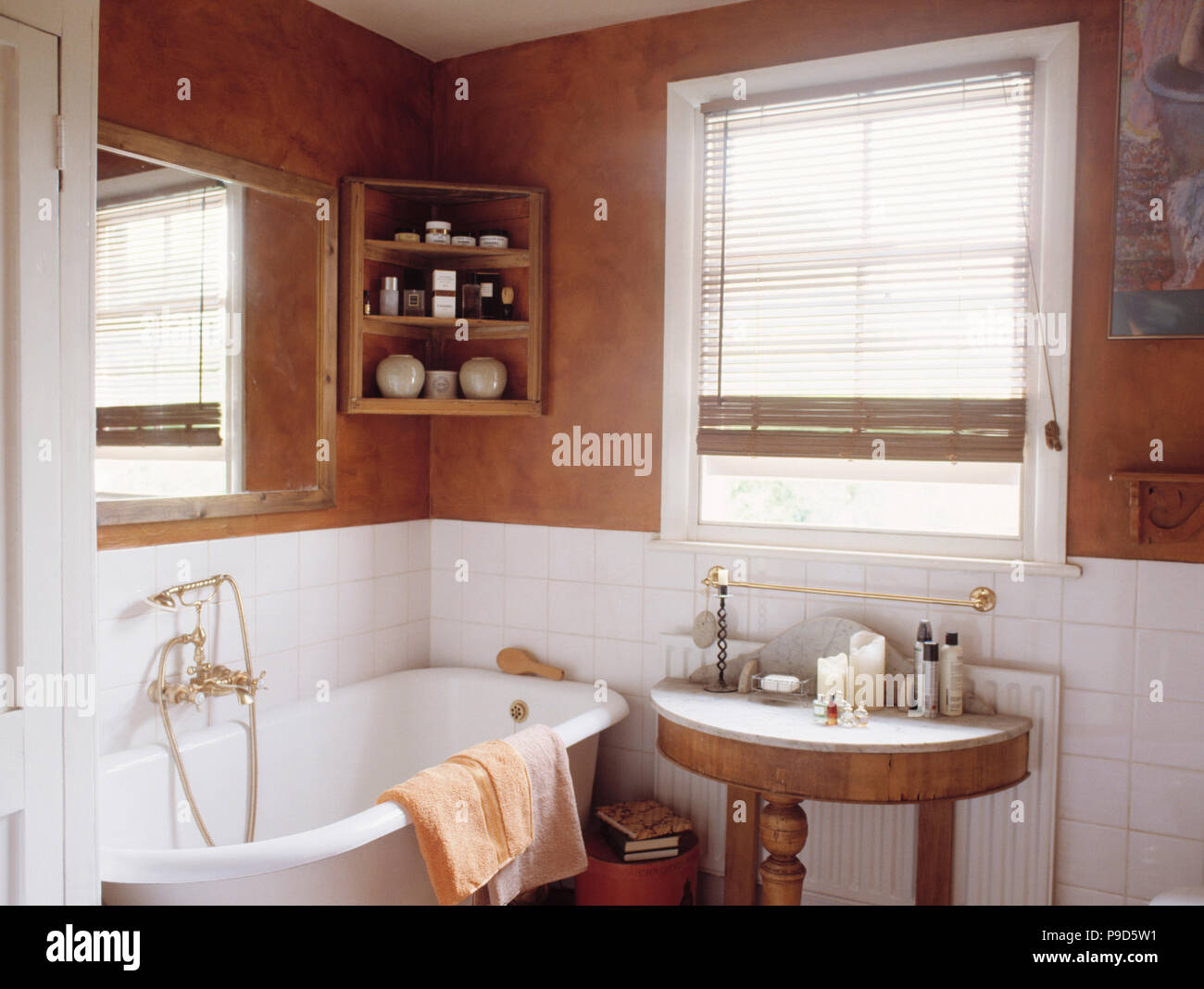 Brown sponge-effect walls above white tiles in bathroom with rolltop bath and small marble-topped antique table Stock Photo