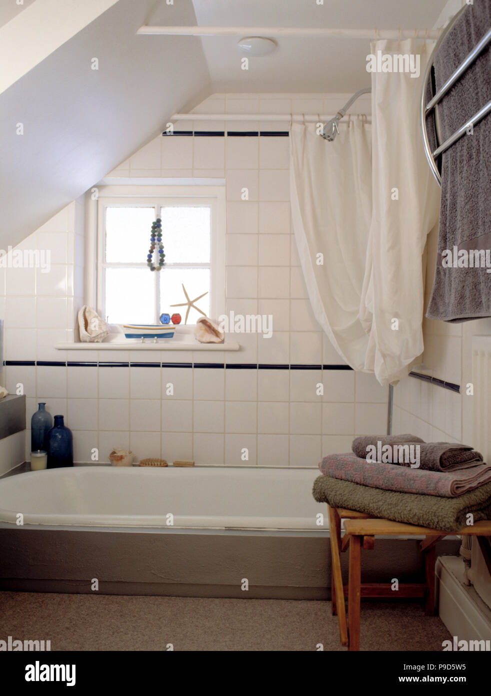 Brown towels on stool beside bath in white tiled attic bathroom Stock Photo