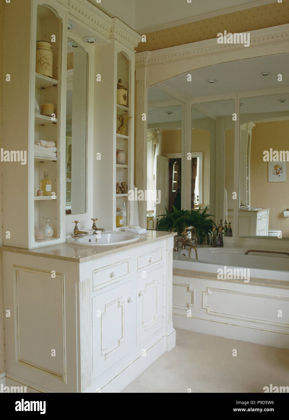 Basin in fitted vanity unit in bathroom with large mirror above bath Stock Photo