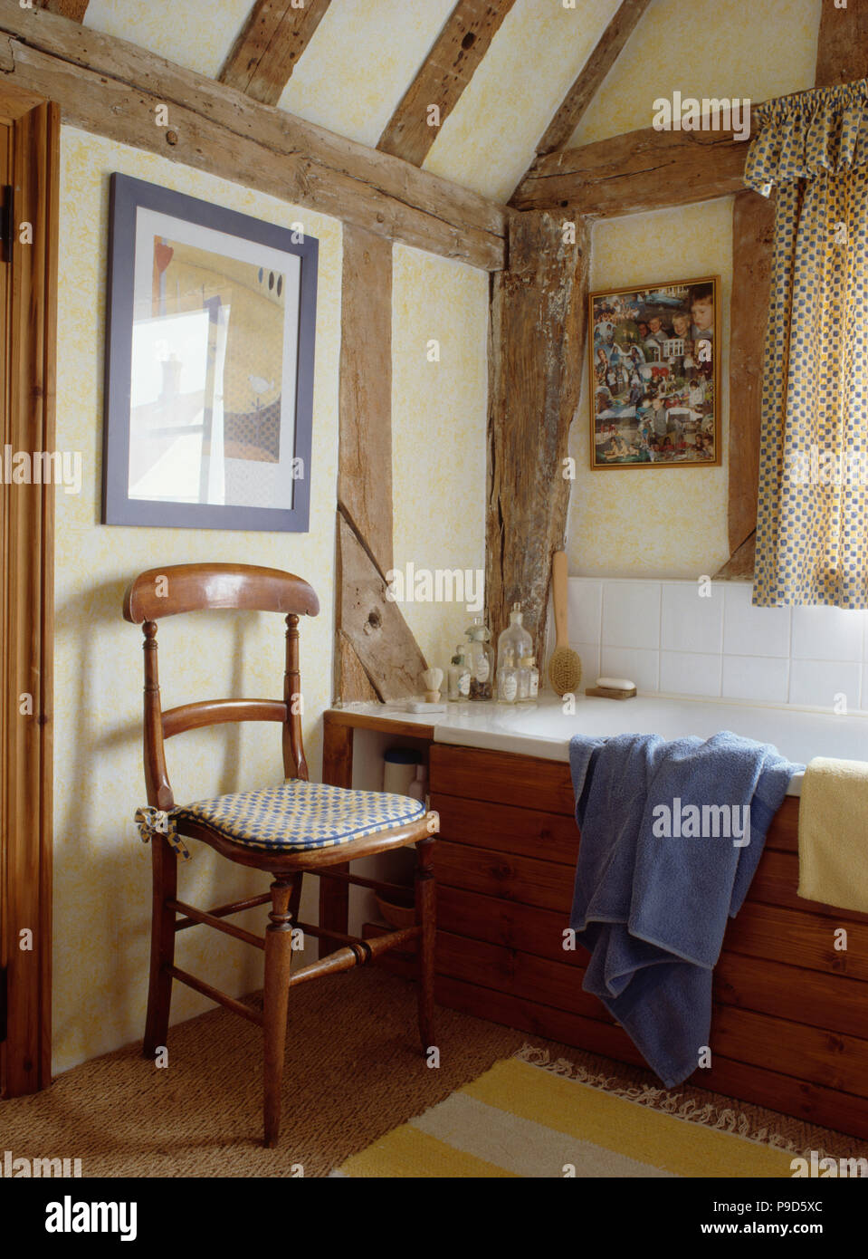 Old wooden chair beside panelled bath in beamed cottage bathroom Stock Photo