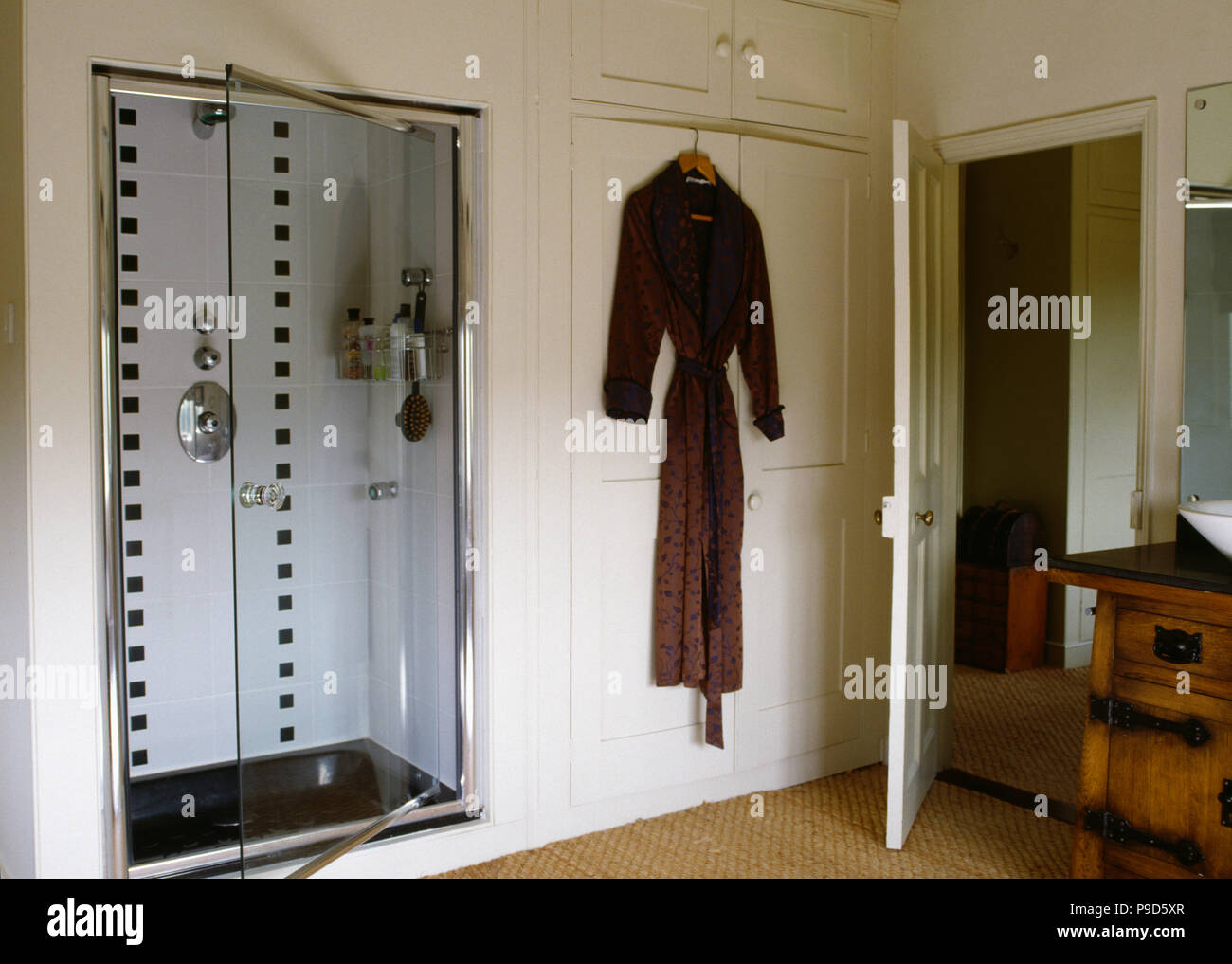 Glass door on alcove shower in cream country bathroom with brown towelling bathrobe on cupboard door Stock Photo