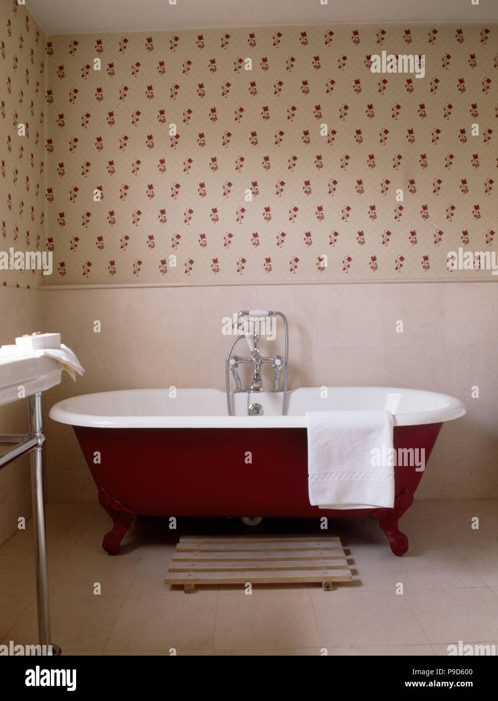 Red roll top bath in traditional bathroom with red sprigged wallpaper Stock Photo