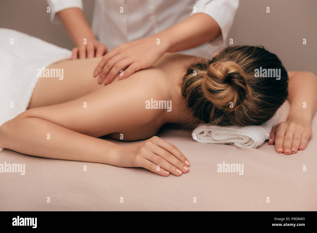 Young smiling woman receiving back massage from a massage professional at beauty salon Stock Photo