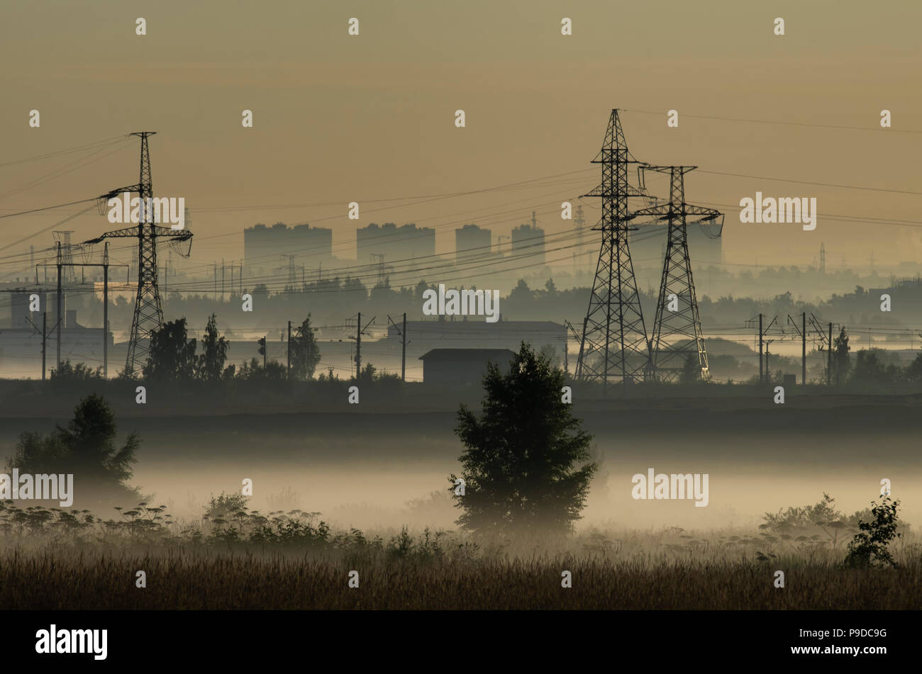 Fog over fields and towers of power lines on the outskirts of the city on the background of power lines Stock Photo