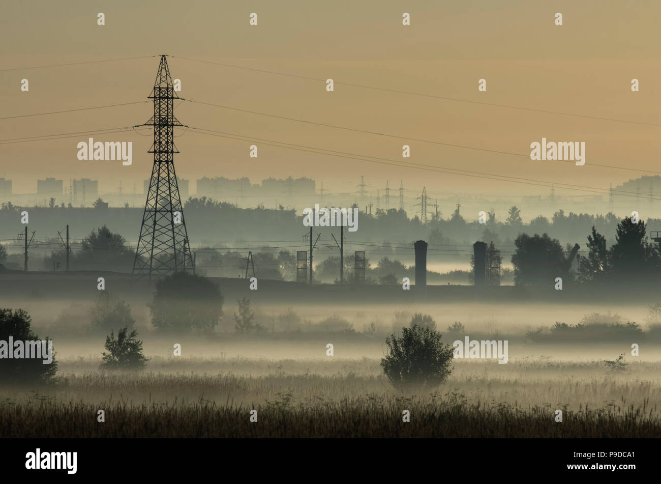 Fog over fields and tower of power lines on the outskirts of the city on the background of power lines Stock Photo