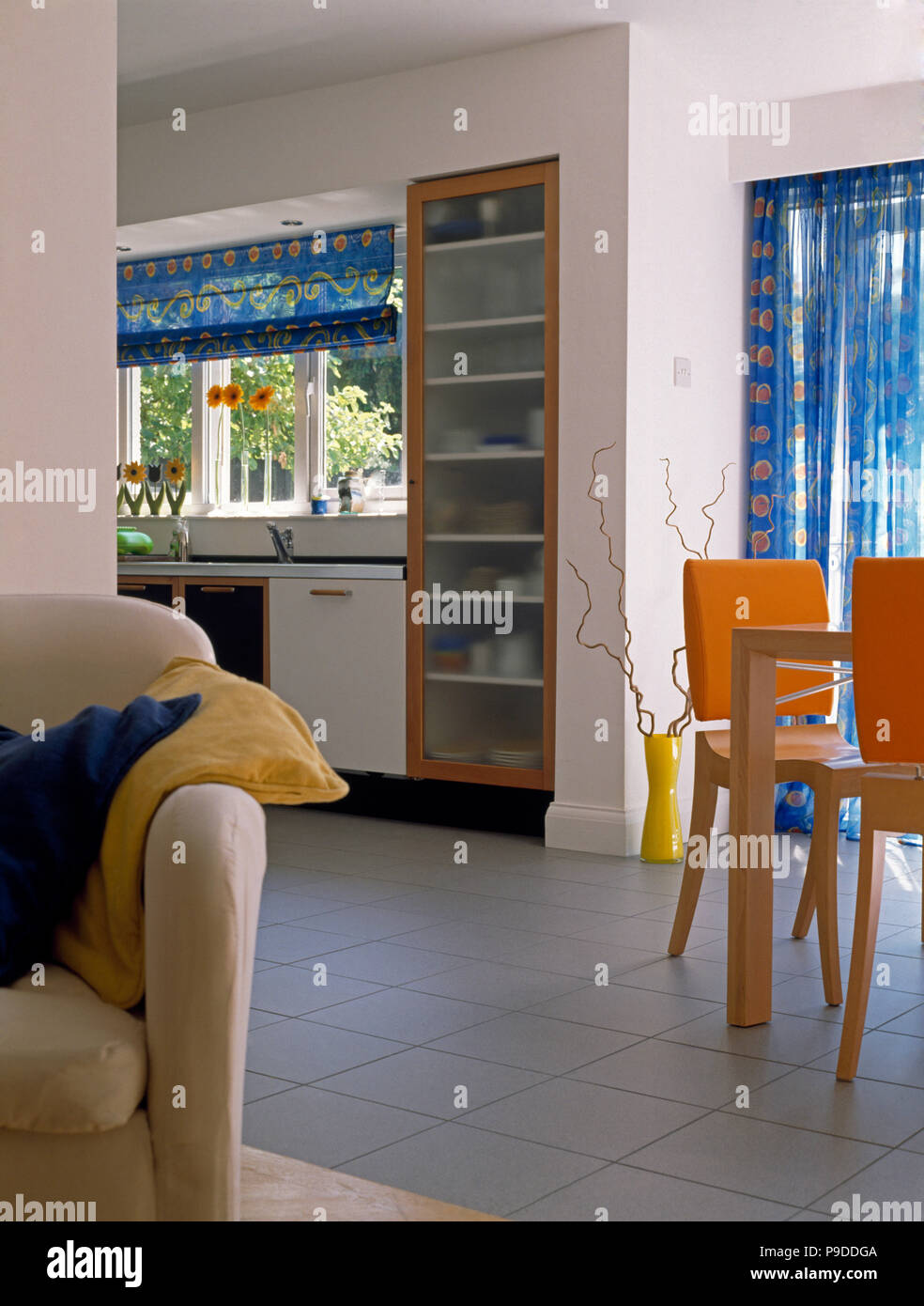 White tiled floor in an open plan kitchen dining room with orange dining chairs and a cream sofa