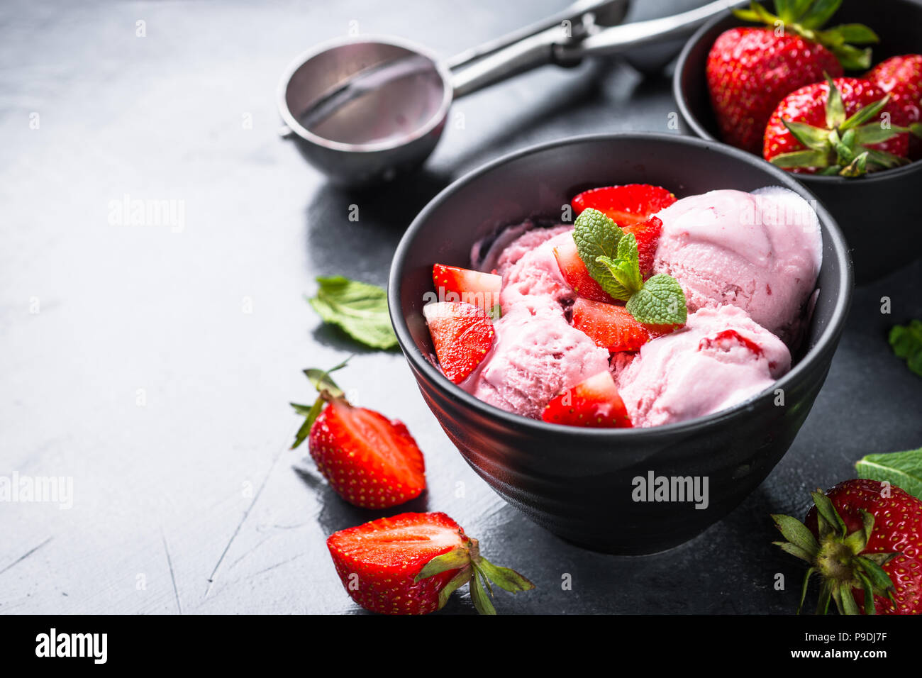 Strawberry ice cream with fresh berries in black bowl. Close up Stock