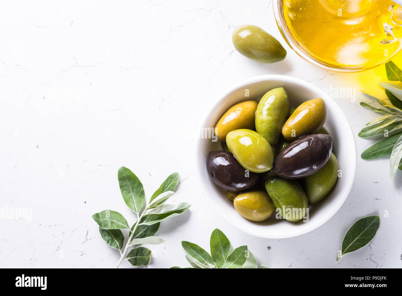 Black and green olives in a bowl and olive oil bottle on white marble ...