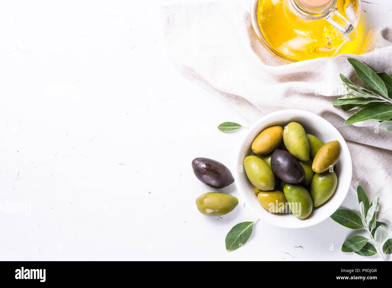 Black and green olives in a bowl and olive oil bottle on white marble ...