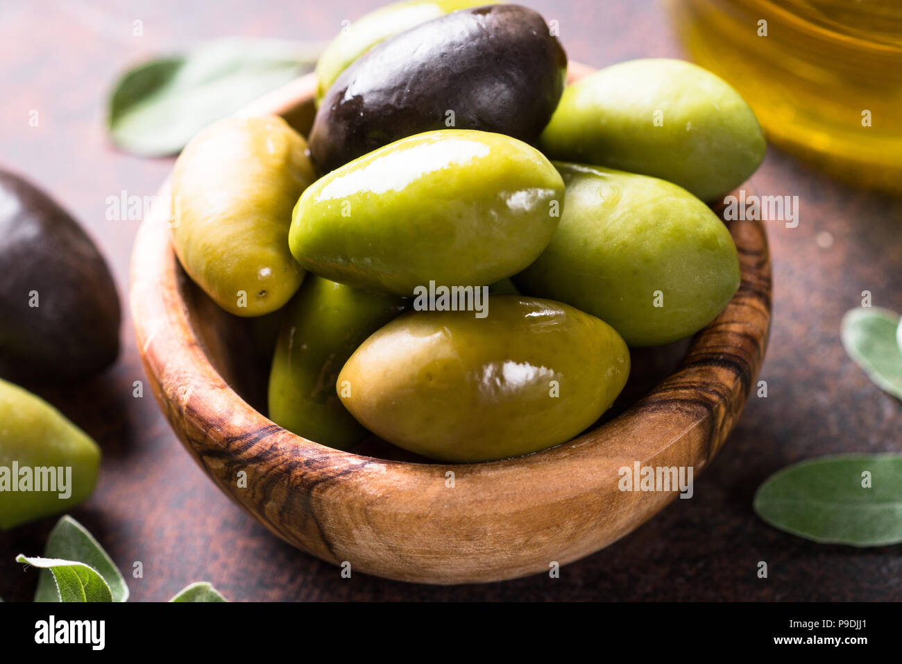Black and green olives in a bowl and olive oil bottle on dark stone ...