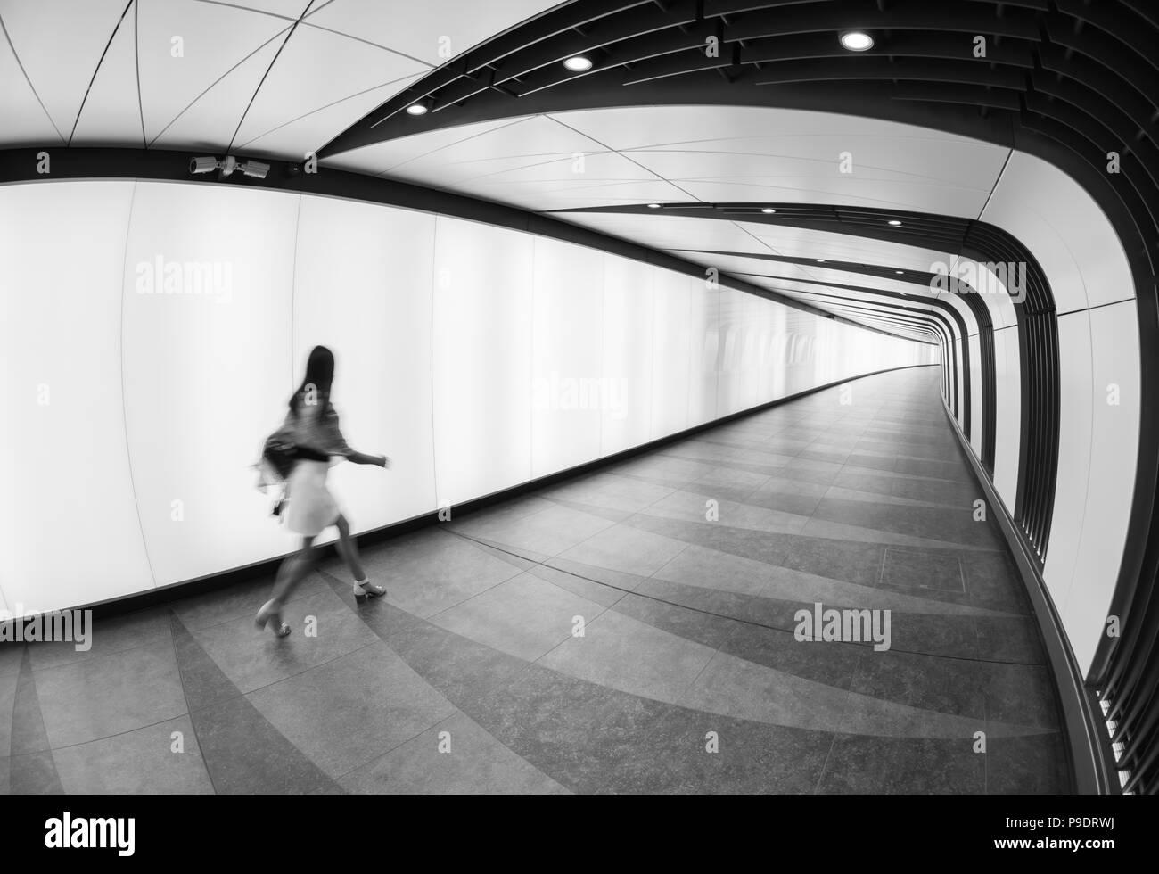 Woman walking in the lit-up tunnel connecting St Pancras International and King's Cross stations in London Stock Photo