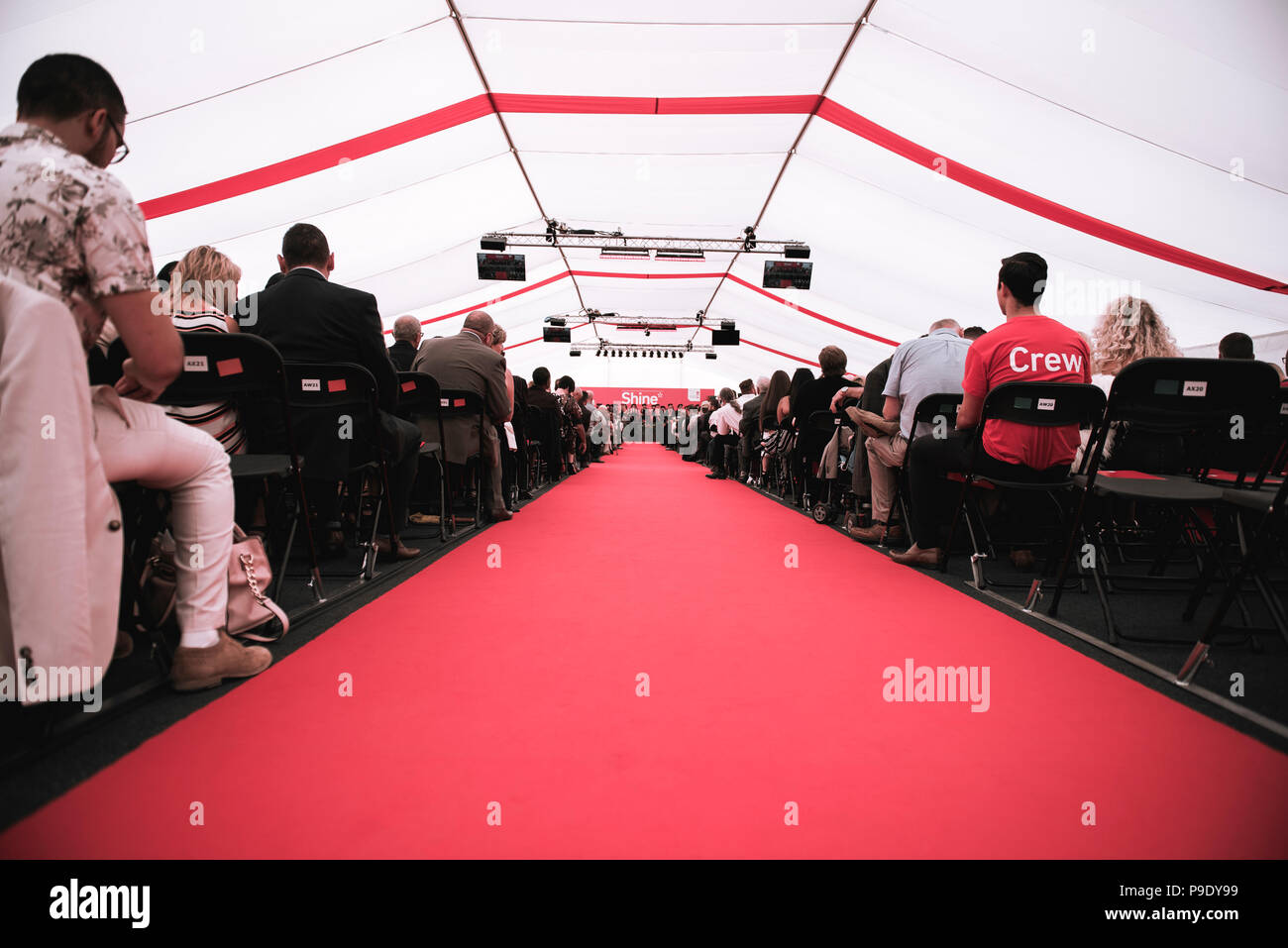 A red carpet leading up to the graduation stage with people sitting on chairs either side. Stock Photo