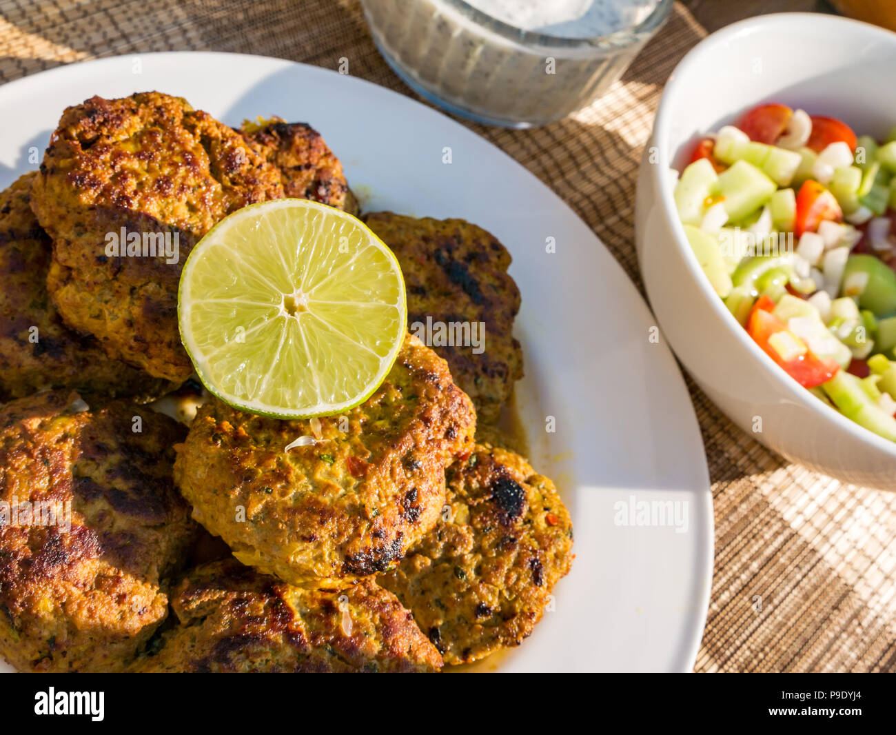 MIddle Eastern food with lamb patty kebabs with half a lime, cucumber and tomato salad and yoghurt herb dressing Stock Photo