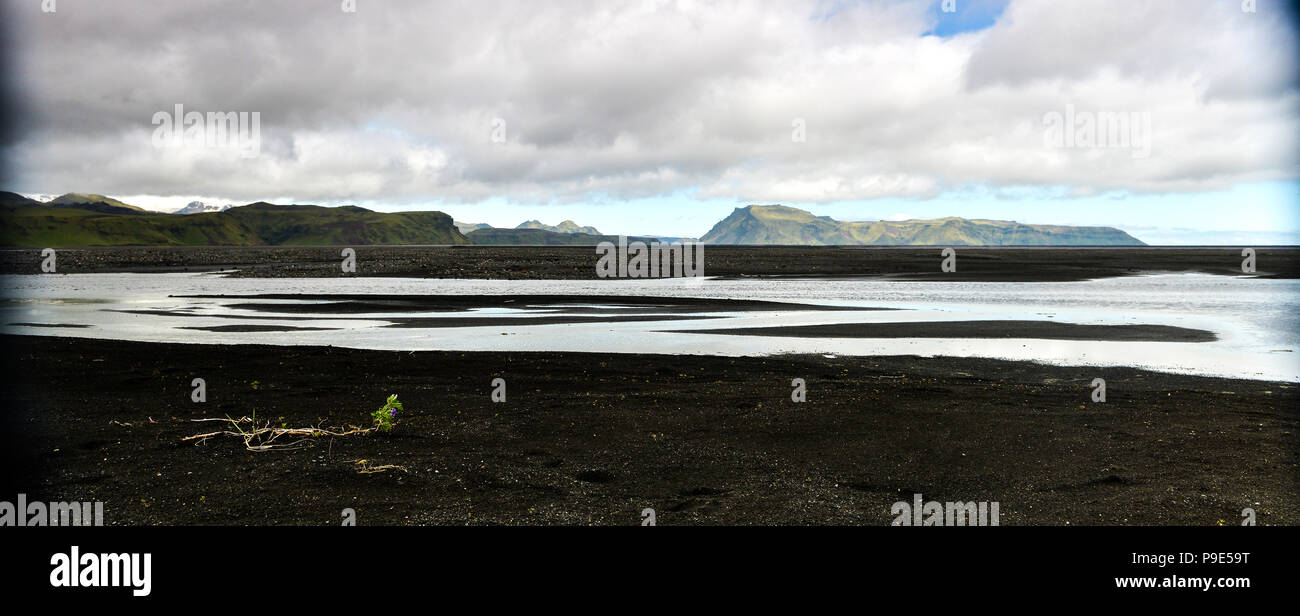 An icelandic landscape of black sand and distant mountains with in the fore ground a river Stock Photo