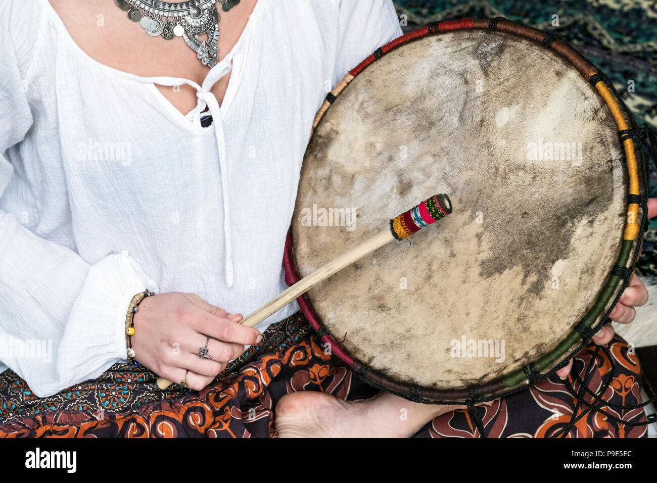 High angle view of woman wearing trousers with floral pattern sitting on shag carpet, holding shaman drum. Stock Photo
