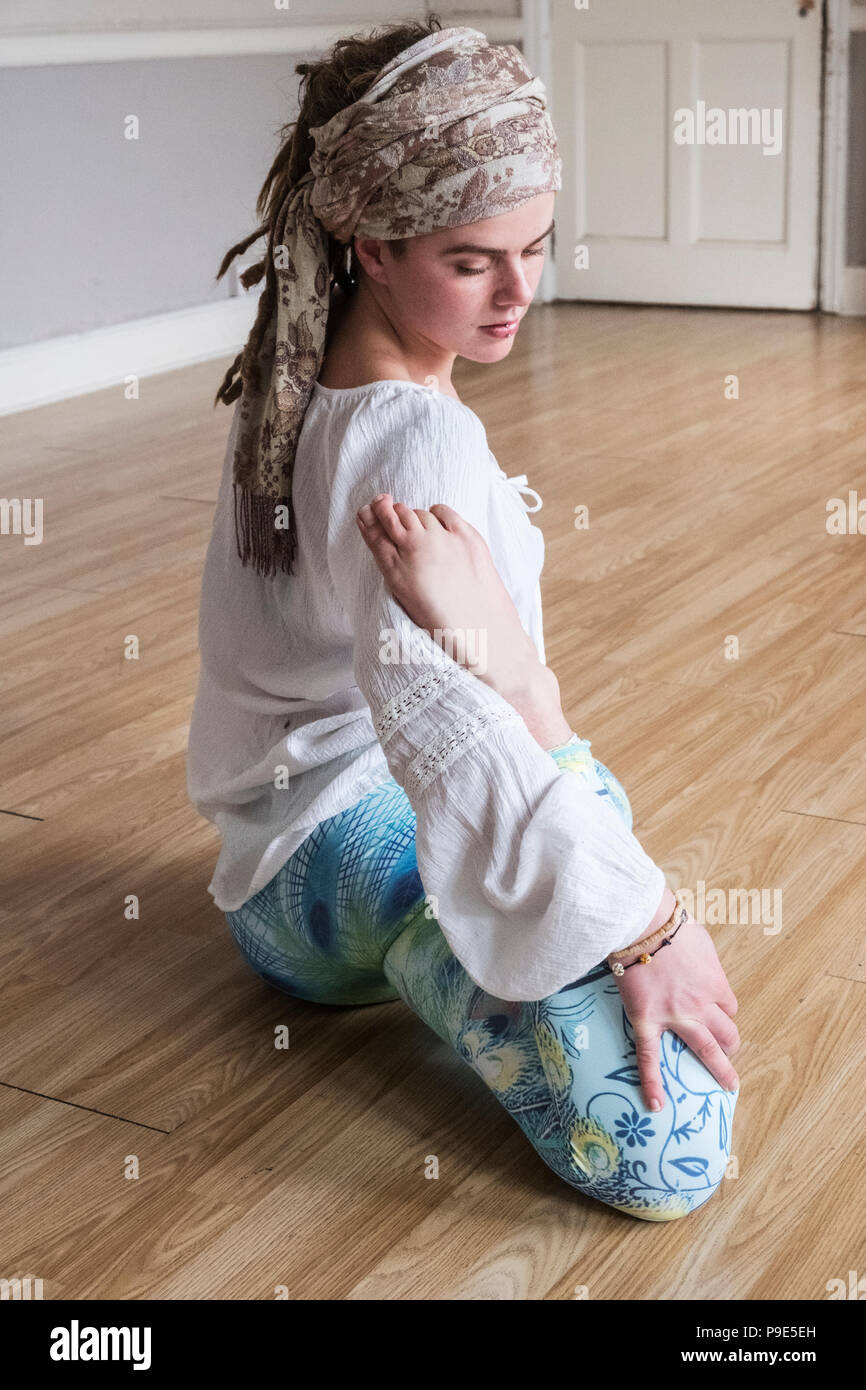 Young woman wearing headscarf and white blouse sitting on floor in yoga pose. Stock Photo