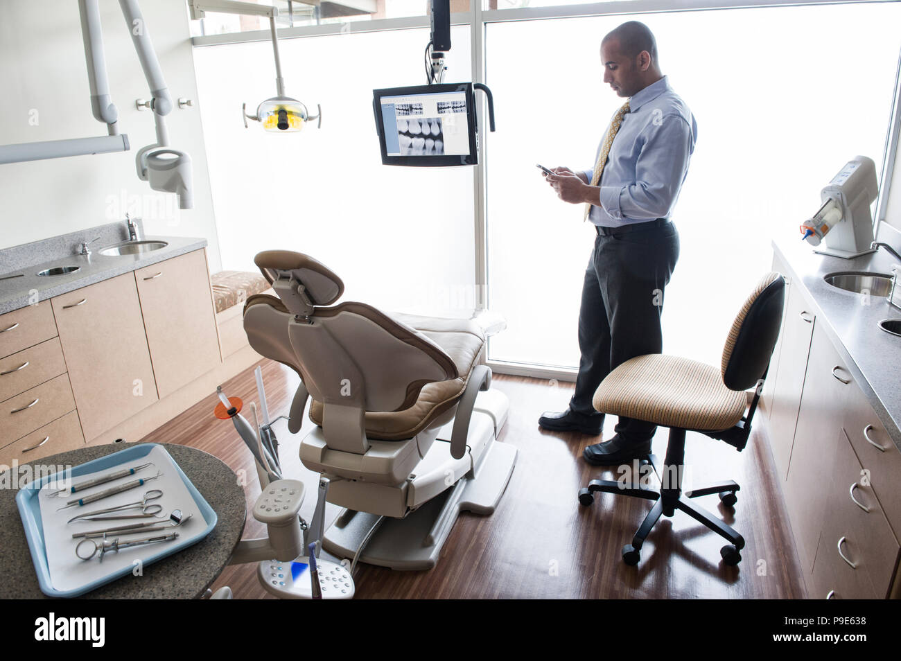A Middle Eastern male dentist checking his cell phone in a dental examination room Stock Photo