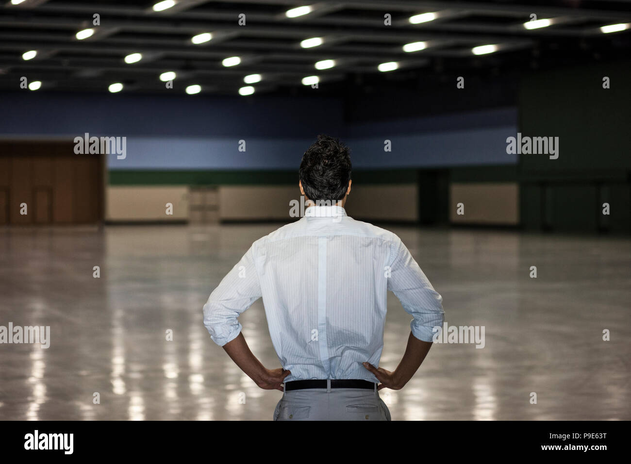 A businessman standing in a dimly lit and dark exhibition area in a convention center. Stock Photo